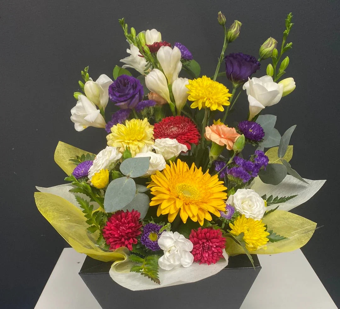 Colorful flower arrangement in a black vase with yellow, red, purple, white, and orange blooms, greenery