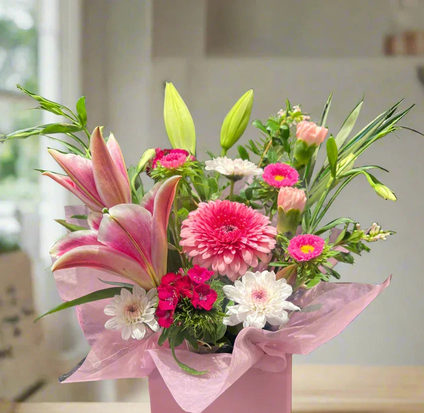 Bright pink and white floral arrangement with lilies, gerberas, carnations in pink box with pink wrapping paper