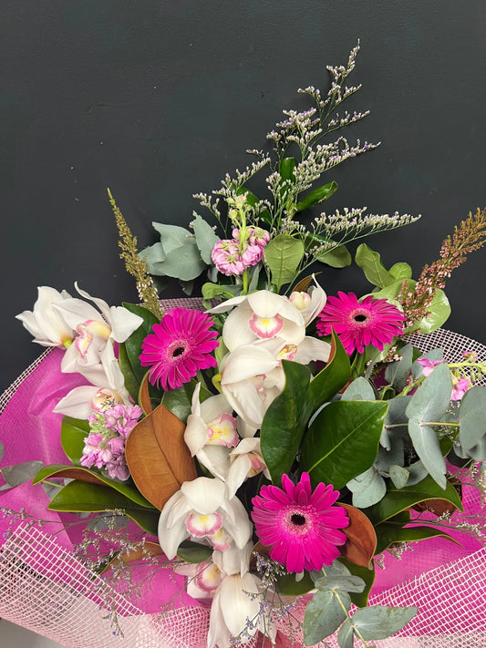 Bright pink gerbera daisies and white orchids bouquet with mixed green foliage on dark background