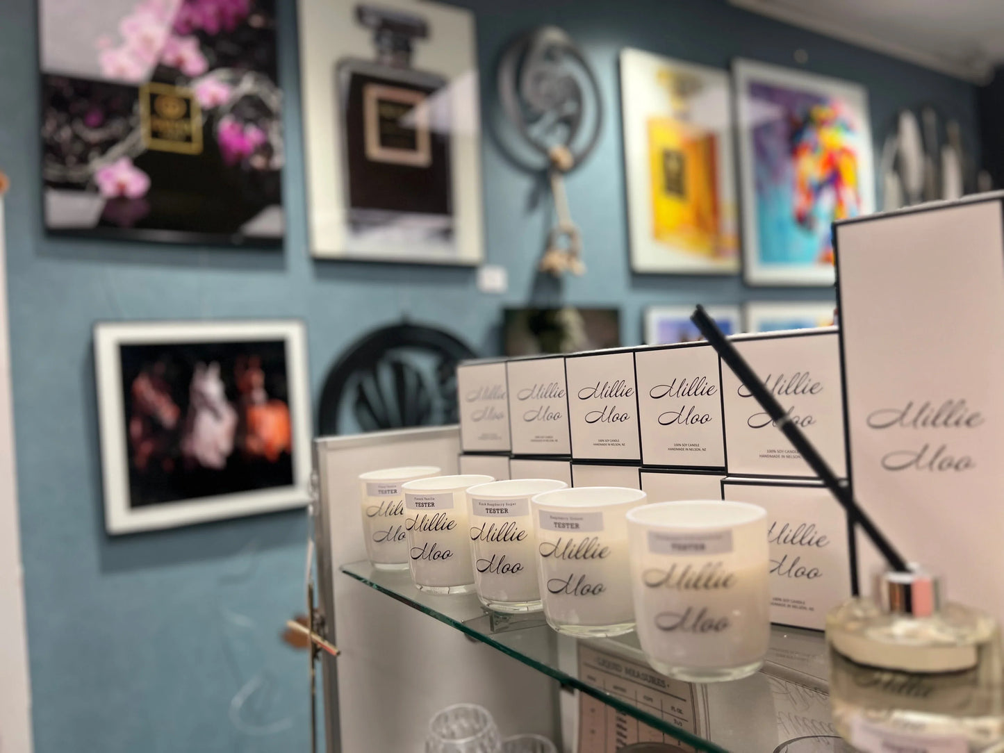 Display of Millie Moo soy candles and diffuser with framed colorful art on blue wall background