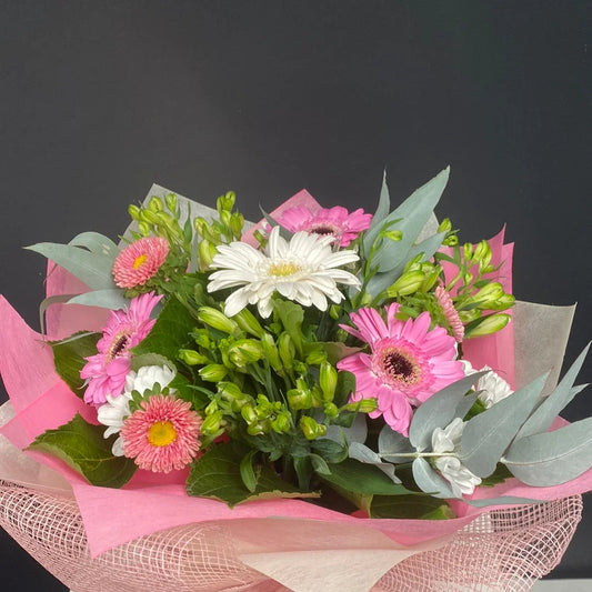 Bouquet of pink and white gerbera daisies with green foliage wrapped in pink and beige paper