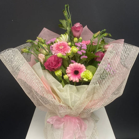 Elegant bouquet of pink and white flowers wrapped in mesh and tissue paper with a pink ribbon bow on black background
