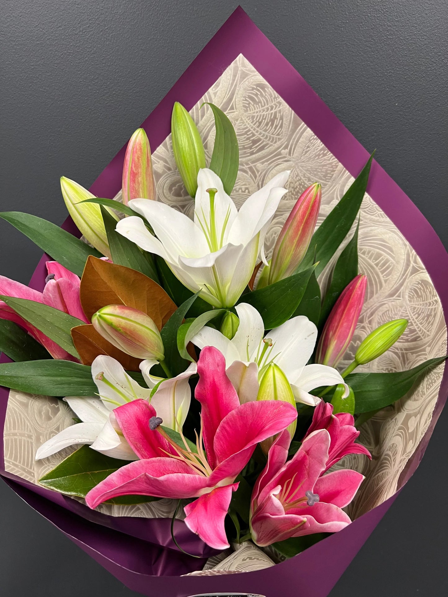 Bouquet of white and pink lilies with green leaves wrapped in purple and patterned beige paper