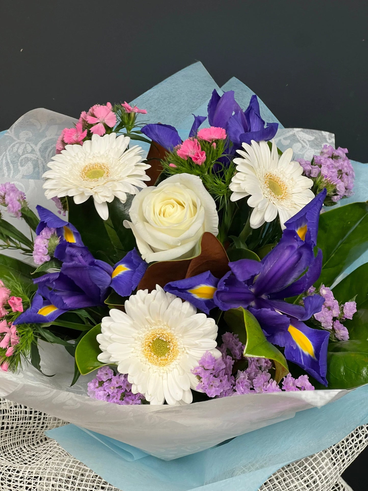 Elegant bouquet with white rose, white gerbera daisies, purple irises, pink and purple fillers wrapped in blue and white paper
