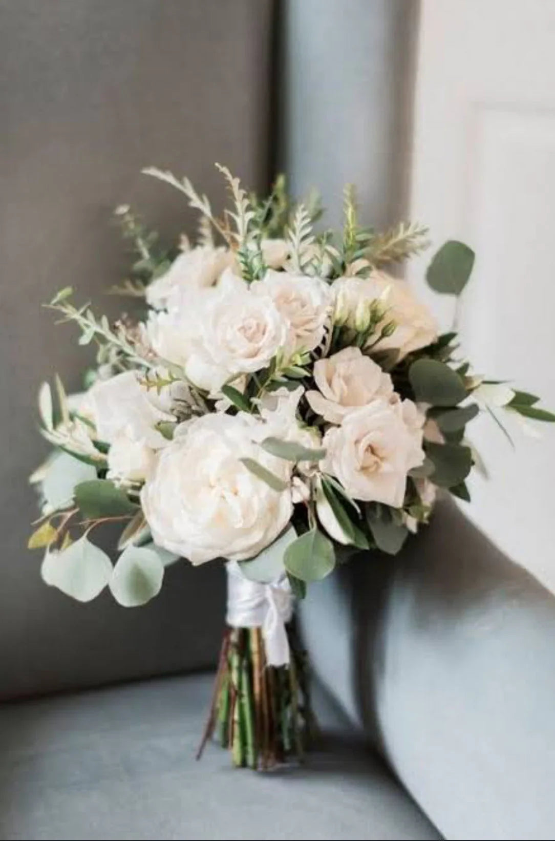 Elegant bouquet of white roses and greenery arranged in a natural style, resting on a soft gray surface