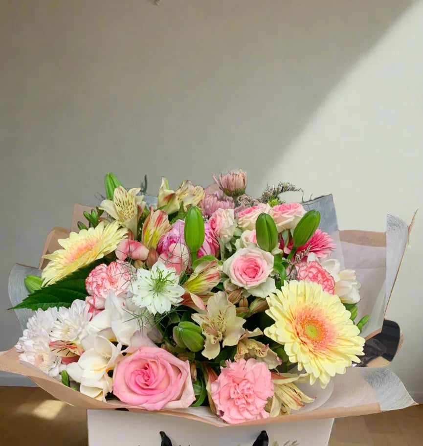 Mixed pastel flower bouquet with pink roses, yellow gerbera, lilies, carnations, and greenery in wrapping