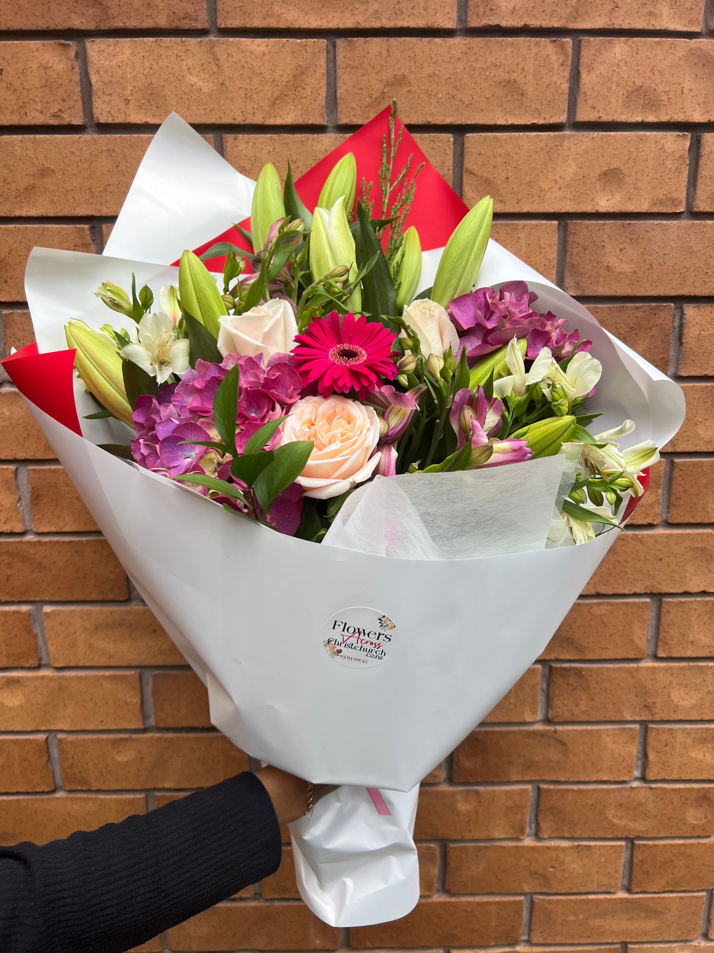 Bouquet of flowers wrapped in white paper held against a brick wall.