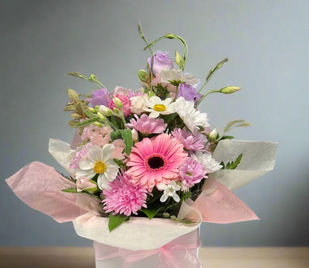 Pastel bouquet with pink gerbera, white daisies, purple lisianthus, and delicate greenery on neutral background