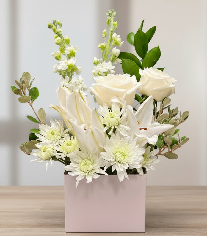 Elegant white floral arrangement with roses, lilies, chrysanthemums, and greenery in a white vase