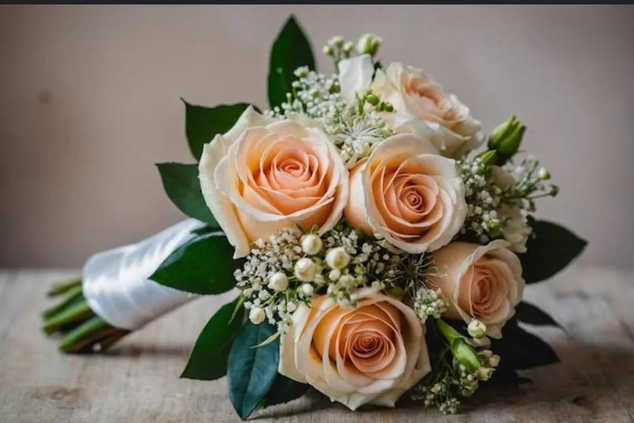 Elegant bouquet of peach roses with greenery and white baby's breath flowers wrapped in white ribbon