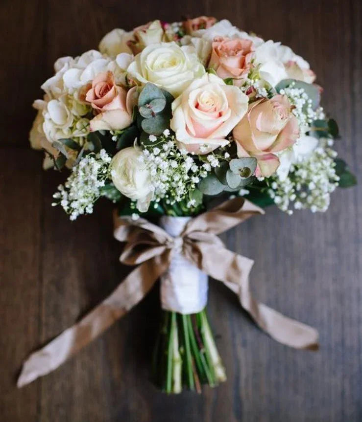 Elegant bridal bouquet with white and peach roses, eucalyptus, and baby's breath tied with a beige ribbon