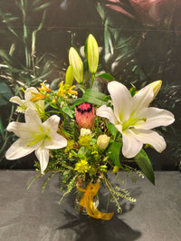 Bouquet of white lilies and greenery in a clear vase on a dark surface.