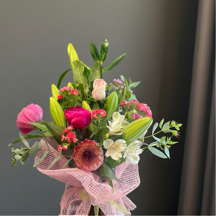 Bright mixed flower bouquet with pink peony, white lilies, pink rose, and tropical greenery wrapped in pink mesh