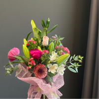 Bright mixed flower bouquet with pink peony, white lilies, pink rose, and tropical greenery wrapped in pink mesh