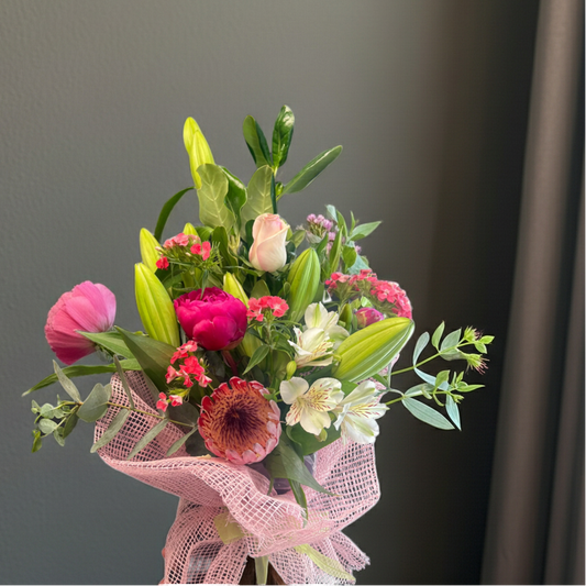 Bright mixed flower bouquet with pink peony, white lilies, pink rose, and tropical greenery wrapped in pink mesh